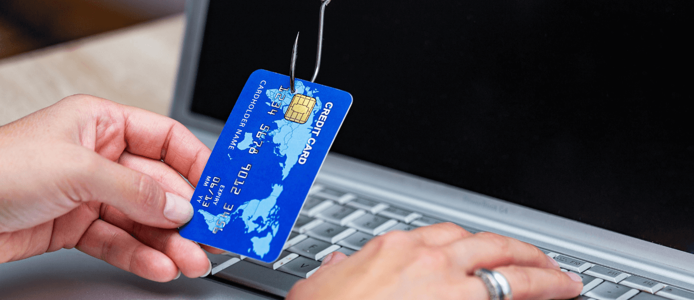 Hands on a laptop covered by a credit card on a hook with a phishing scam targeting personal information