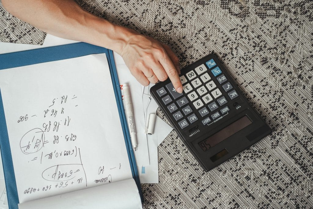 typing on a calculator with notebook pages nearby on light grey surface.