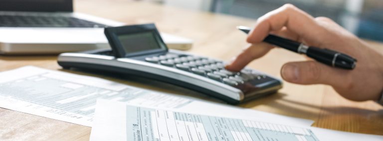 Hand Typing on Calculator on Wood Table Top with Tax Documents Nearby