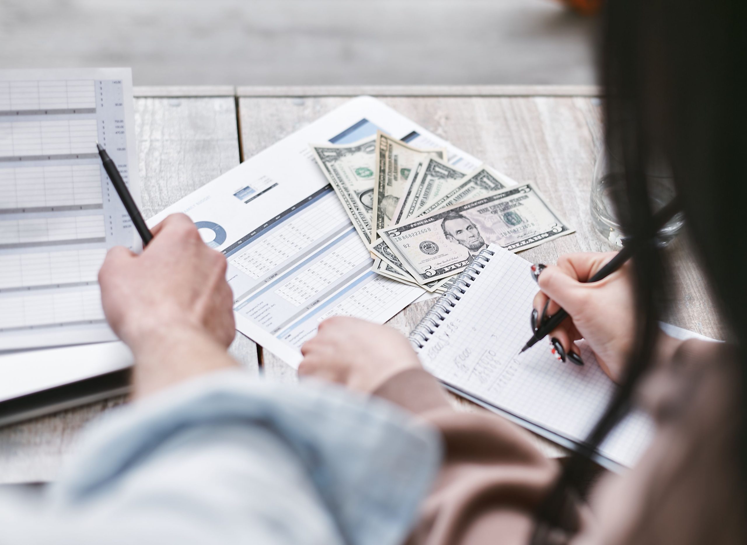 woman doing man on notebook pages with cash and budget sheets nearby on wooden surface.