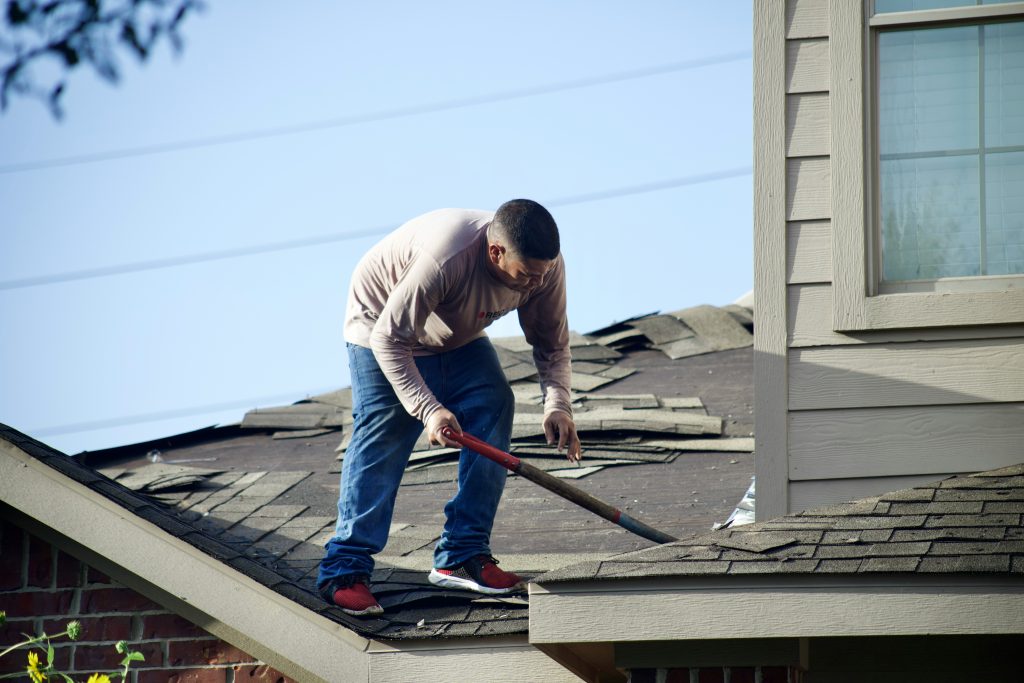 Man standing up repairing roof on residential home.