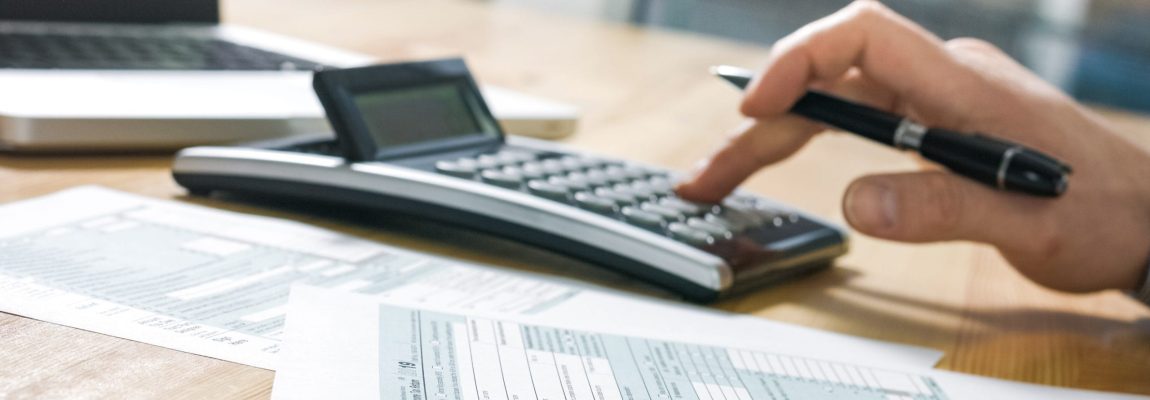 Hand Typing on Calculator on Wood Table Top with Tax Documents Nearby