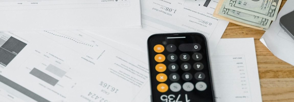 Man writing on financial documents with cash and a calculator nearby on a light wooden surface.