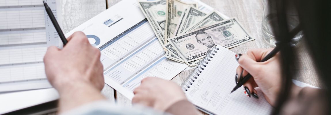 woman doing man on notebook pages with cash and budget sheets nearby on wooden surface.