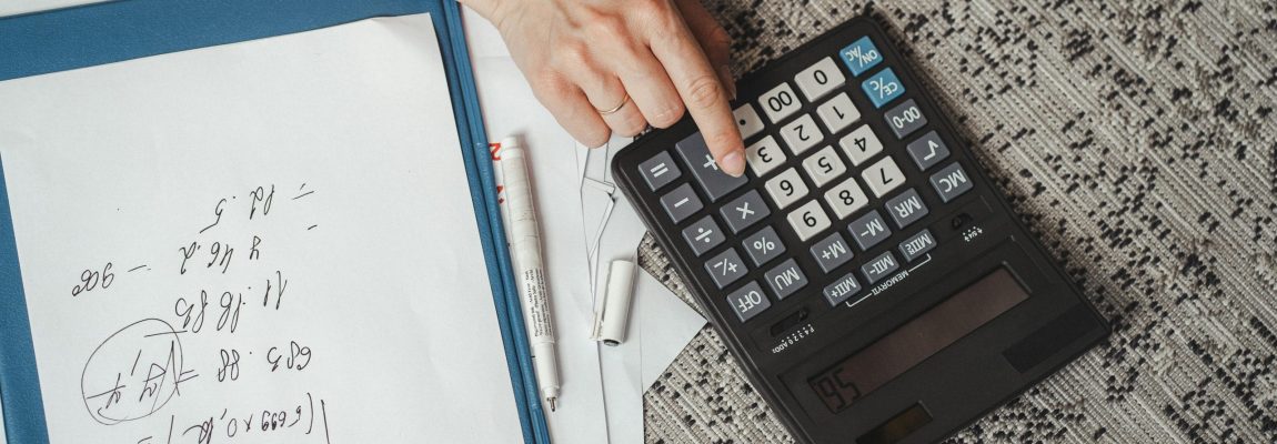typing on a calculator with notebook pages nearby on light grey surface.