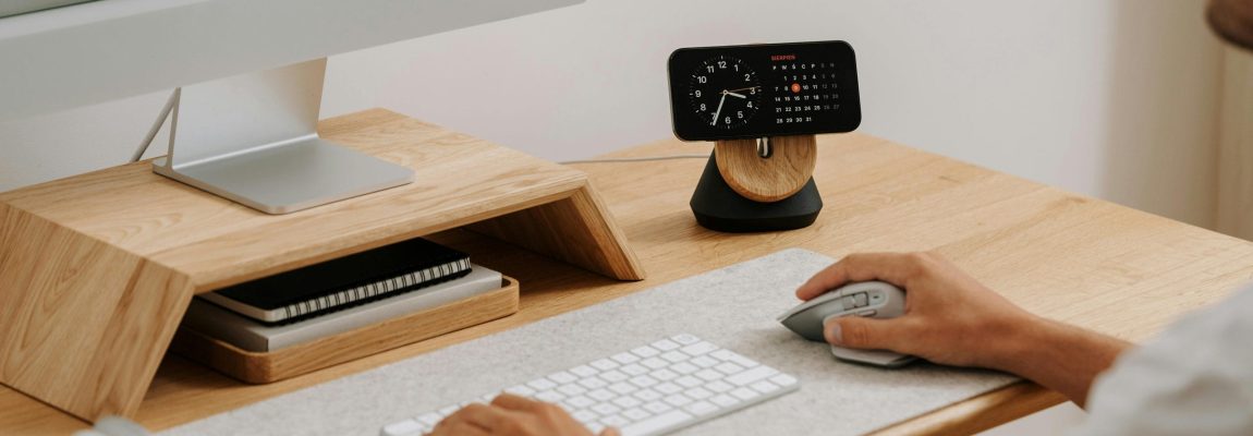 Man sitting at modern, wooden desk typing on keyboard and working on desktop computer.