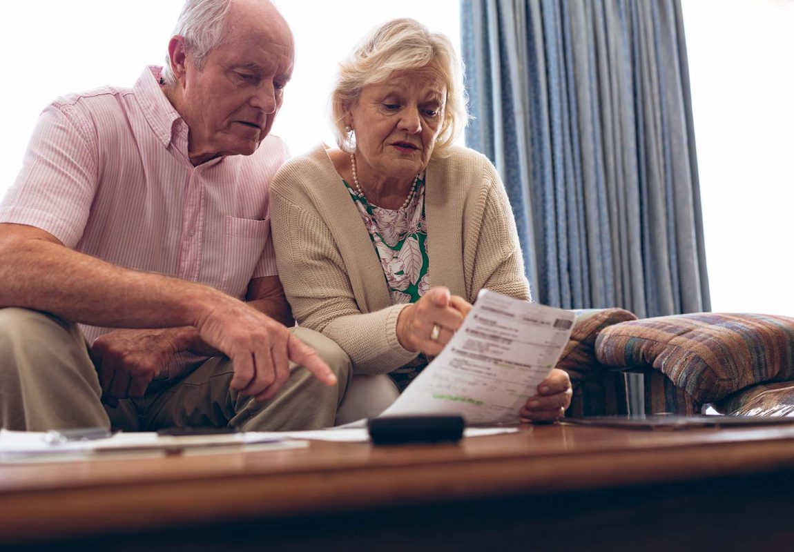 an older couple sitting down looking at a document inside a home in bright light