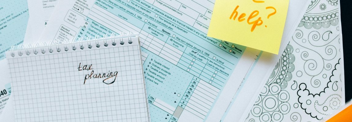 white and light blue tax documents layed out on a table top with a yellow sticky note and red pen writing.